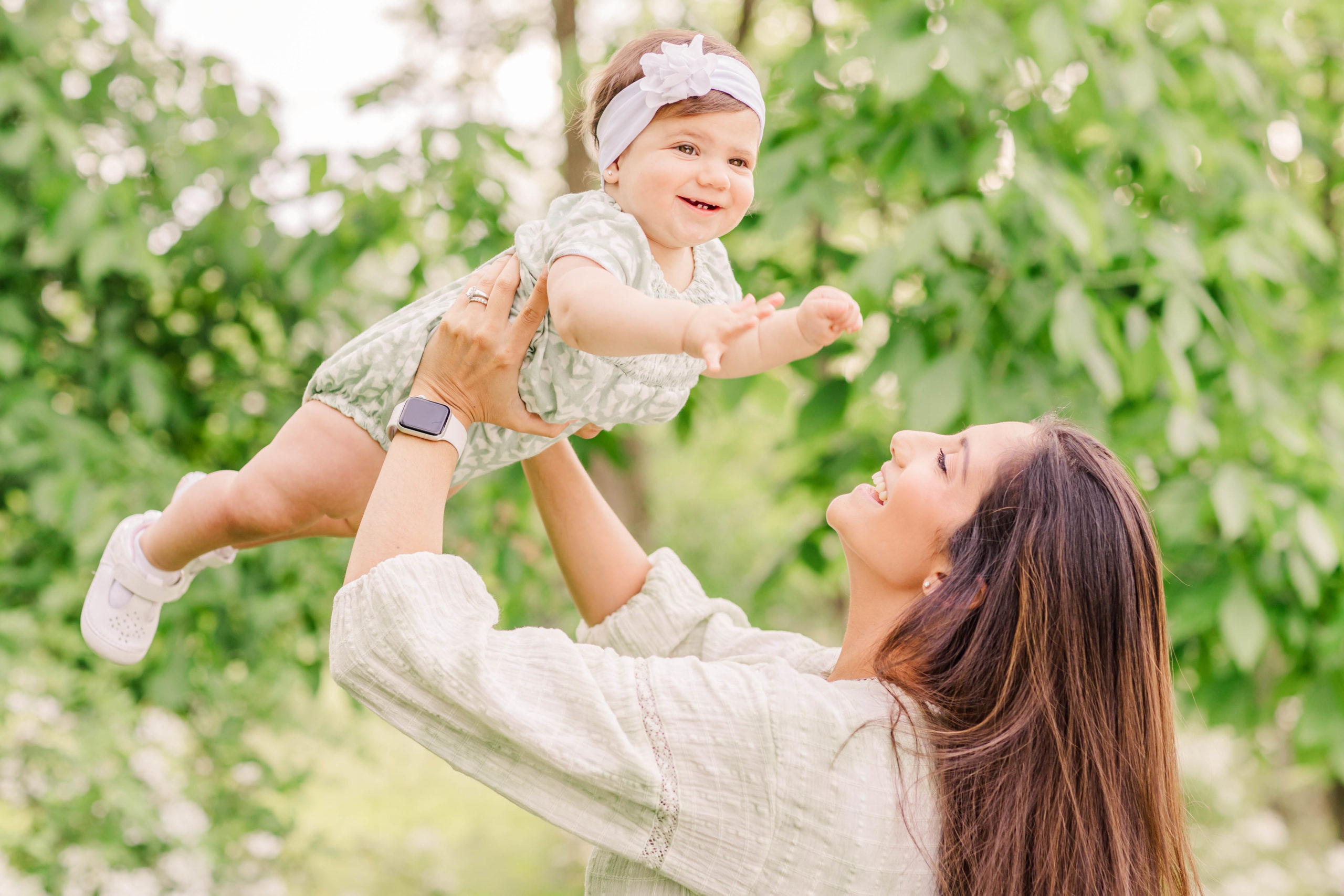 A little girl lifted up against the beautiful airy green foliage, at this mommy and me session.