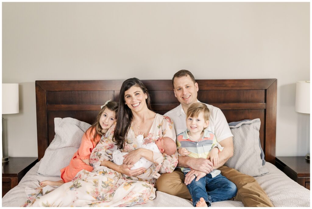 Parents and three kids sitting on a bed during lifestyle newborn session