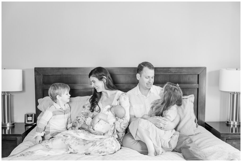 Black and white image of family of five sitting on a bed during lifestyle newborn session