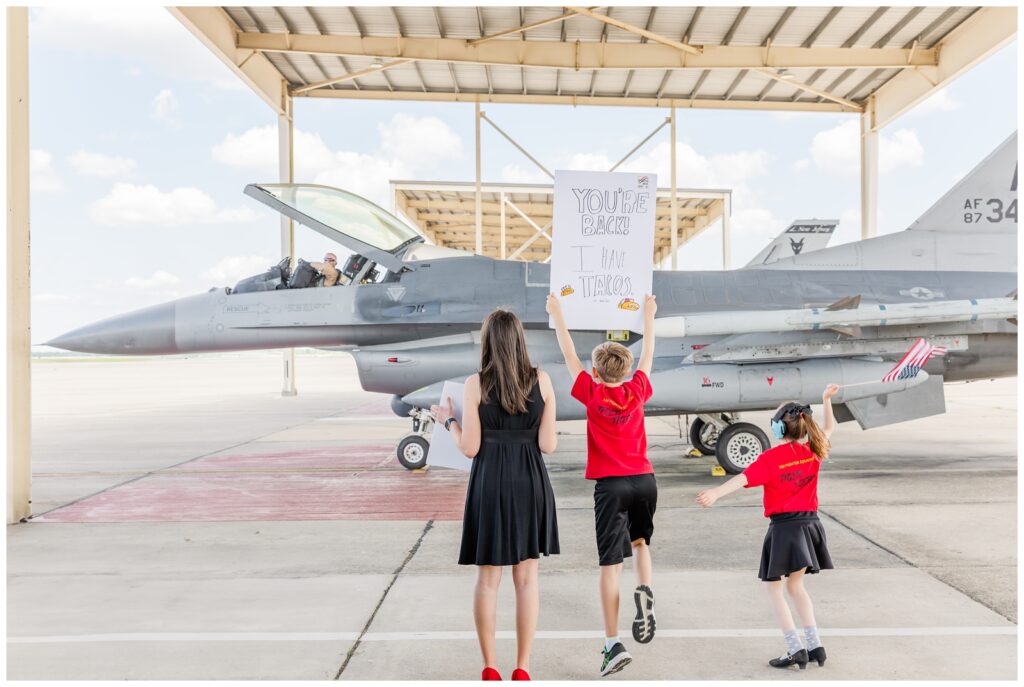 Family holding signs and waving flags while dad get's out of an F-16