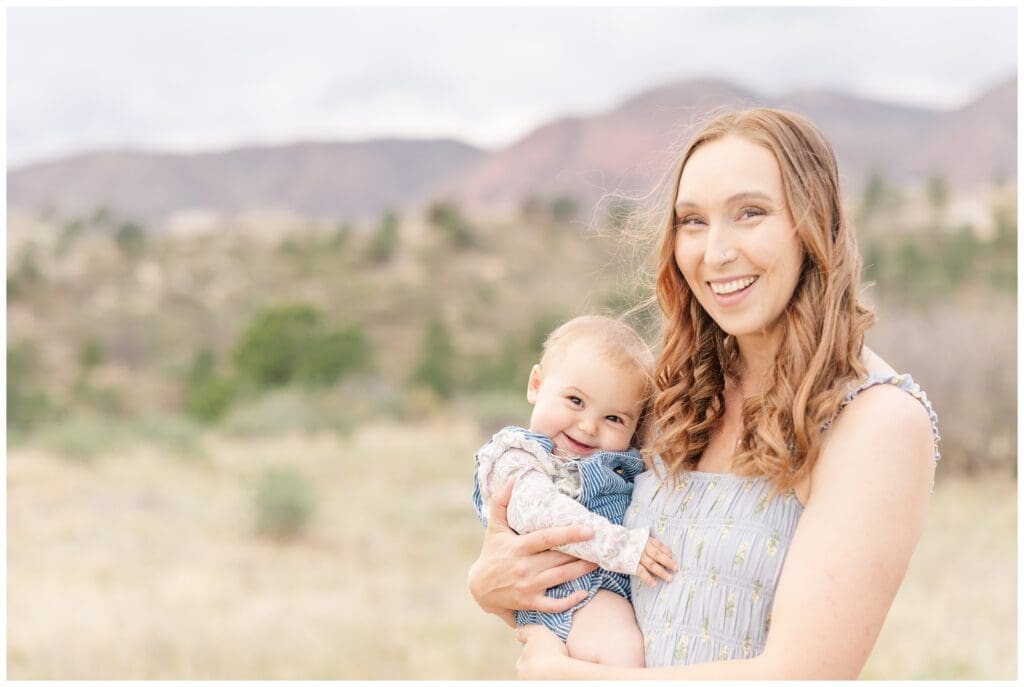 Mom holding her smiley baby girl with mountains in the background
