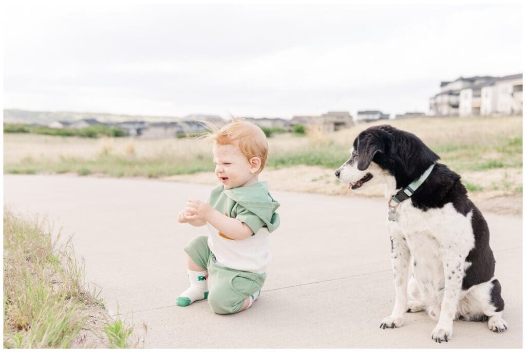 Toddler sitting on the sidewalk with his dog